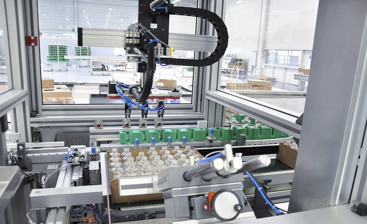 Robot cartesiano con pinza en botellas, bandejas y transportadores de una línea industrial